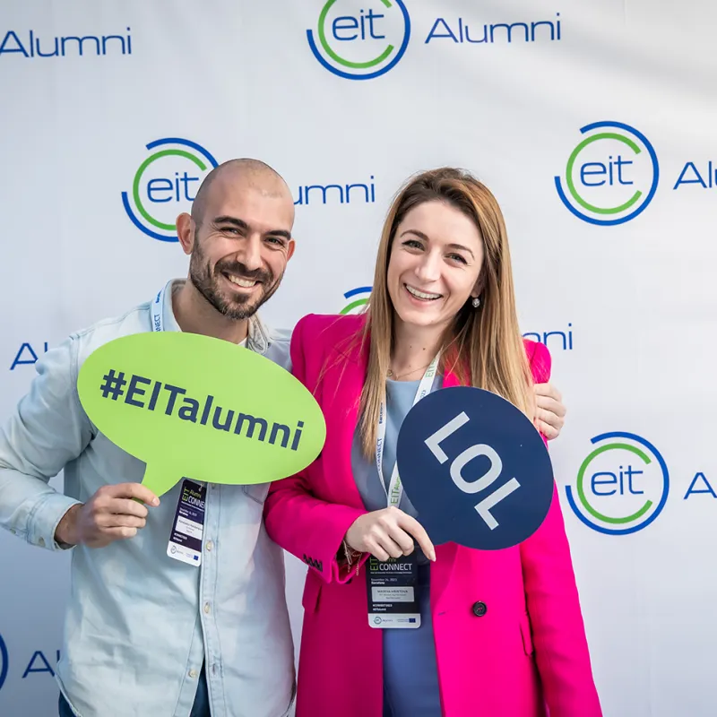 2 people standing in front of EIT alumni picture wall